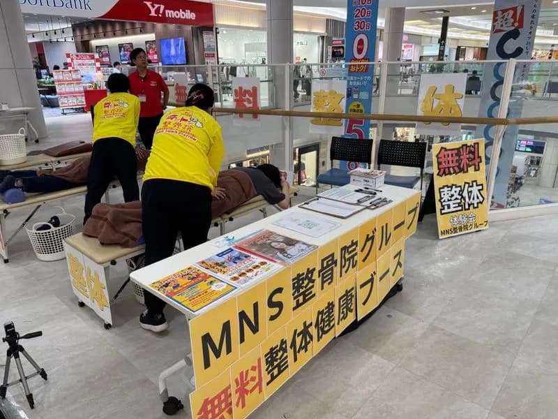黄色いシャツを着た当グループのスタッフが、健康ブースのベッドで来場者の身体をケアしている様子